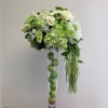 White and green floral arrangement in a tall clear vase with apples inside