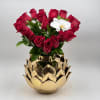 Red roses arranged in a gold lotus-shaped vase with one white orchid bloom