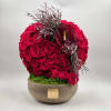 Round arrangement of red roses in a low bowl with a dark anthurium accent