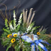 Floral tribute with sunflowers, blue hydrangeas, and blue ribbons on a dark stand