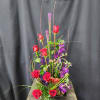 Tall arrangement of red roses and purple flowers in a low black container