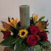 Red roses and orange lilies arranged around a tall candle in a glass bowl