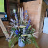 Tall floral arrangement with blue flowers and two fish decorations in a metal bucket