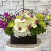 Floral arrangement with orchids, hydrangeas, and green carnations in a dark box