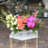 Mixed floral arrangement with roses, orchids, and pink blooms in a white pedestal vase