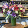 Large mixed bouquet in a tall green vase with pink, purple, red, and yellow blooms