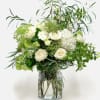 White roses and hydrangeas in a clear glass vase with airy greenery
