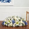 Low floral centerpiece with white lilies, roses, and daisies accented in blue