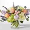 Pastel bouquet of roses, hydrangeas, and purple spikes in a clear glass vase