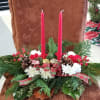 Christmas centerpiece with red candles, white flowers, pinecones, and plaid ribbon