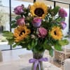 Bouquet of sunflowers and pink roses in a glass vase with a purple ribbon
