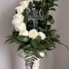 White roses arranged around a clear glass cross on a pedestal stand