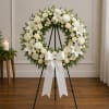 White floral wreath on a black stand with a white ribbon bow