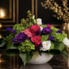 Mixed bouquet of roses, lisianthus, and purple blooms in a white bowl vase
