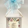 A distressed white decorative lantern topped with a sheer green bow creates