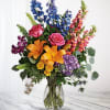 Colorful bouquet with lilies, roses, and tall blue and pink blooms in a glass vase