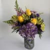 Bouquet of yellow roses, purple hydrangea, and mixed blooms in a glass vase