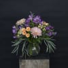 Mixed bouquet of purple, peach, and pink flowers in a glass vase