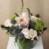 Peach and white roses in a green glass vase with blue thistle and green pom-pom flowers
