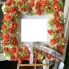 Square floral tribute with orange roses and white flowers on an easel