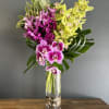 Pink and yellow orchids arranged in a tall glass vase.