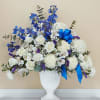Tall white and blue sympathy flower arrangement in a white pedestal vase with a blue bow