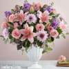 Pink lilies, roses, and purple flowers arranged in a white vase