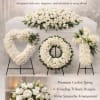 White funeral floral set with casket spray, heart, wreath, cross tributes, and vase bouquet on a soft neutral backdrop.