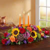 Low floral centerpiece with lit orange candles and mixed roses and sunflowers