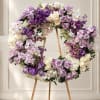 Large circular floral wreath on a wooden easel with purple, white, and cream blooms