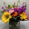 Colorful bouquet with sunflowers, roses, and purple blooms in a glass vase