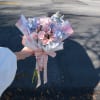Handheld bouquet of pink roses and pale blue flowers wrapped in pastel paper