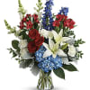 Bouquet of red roses, white lilies, blue flowers, and white blooms in a glass vase