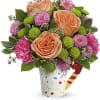 Peach roses and pink flowers in a confetti-patterned cup with a candy cane pick
