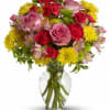 Mixed bouquet of pink roses, red carnations, and yellow daisies in a clear glass vase