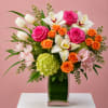 Mixed bouquet of pink roses, white orchids, orange roses, and tulips in a glass vase