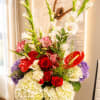 Tall mixed flower arrangement with red roses, white blooms, and purple hydrangeas in a glass vase