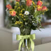 Bouquet of coral tulips and small white daisies in a glass vase with a green ribbon