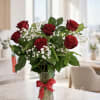 Red roses with white baby's breath in a clear glass vase tied with a red ribbon