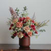 Mixed bouquet of peach roses and burgundy flowers in a brown vase