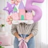 Person holding pastel castle and number 5 balloons with flowers