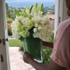 White floral arrangement in a clear glass vase being held at a doorway