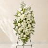 White funeral spray on a standing easel with lilies, roses, and hydrangeas
