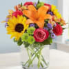 Colorful bouquet with sunflowers, lilies, and roses in a clear glass vase