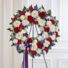 Circular wreath of red, white, and blue flowers on a stand with ribbon
