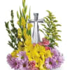 Yellow gladiolus and purple daisies arranged around a silver bottle
