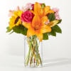 Bouquet of orange lilies, a pink rose, and a sunflower in a glass vase