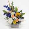 Mixed bouquet in a gray square vase with blue, white, yellow, and peach flowers