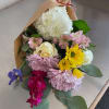 Mixed bouquet of white, pink, yellow, and purple flowers wrapped in brown paper