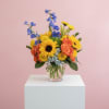 Bright sunflowers, roses, and seasonal blooms arranged in a clear glass vase.